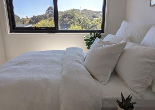 Cama blanca con almohadas blancas y ventana en The Botanical 301 en Albury