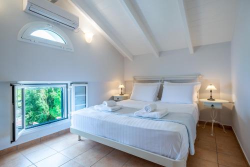 a white bedroom with a large bed and a window at Meganisi Villas in Spartokhórion