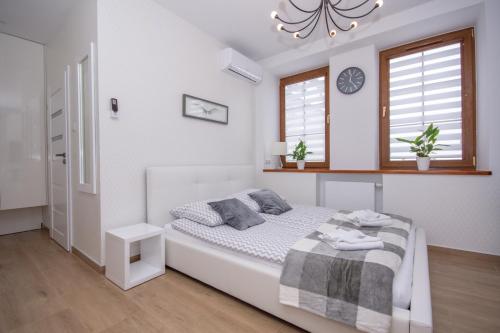 a white bedroom with a bed and two windows at Apartamenty AP 10 in Częstochowa
