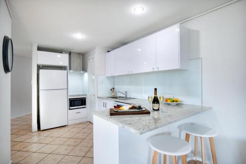 a white kitchen with white appliances and stools at Heart of Airlie Beach Apartment in Airlie Beach