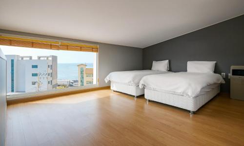 two beds in a room with a large window at Pampas Hotel Jeju in Jeju