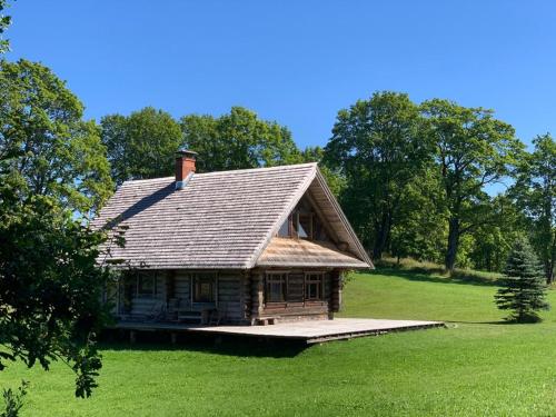 an old house with a roof on a green field at Vucini in Andzeļi