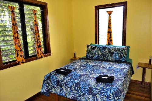 a bedroom with a bed with blue sheets and two windows at Iguana Roost Tourism Gold Standard Fully Equipped two Bedroom Cabin in San Ignacio