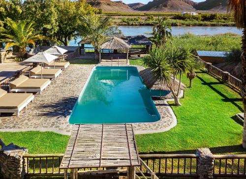 a swimming pool in a resort with a river at Orange River Rafting Lodge in Kotzeshoop