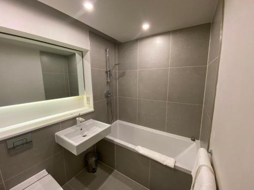 a bathroom with a sink and a tub and a mirror at Axiom Park Hotel in London