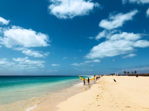 two people standing on a beach with a surfboard at Agua Hotels Sal Vila Verde in Santa Maria