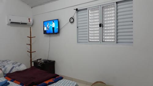 a bedroom with a tv on the wall and a window at Pousada Catarina in Maringá