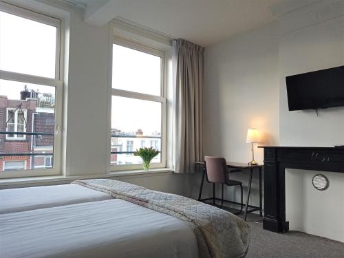 a bedroom with a bed and a desk and two windows at Hotel Verdi in Amsterdam
