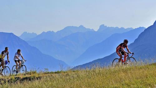three people riding bikes on a hill with mountains in the background at SOWELL RESIDENCES Pra Loup in Pra-Loup