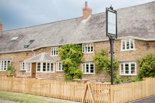 un edificio de ladrillo con un cartel delante en The Red Lion at Hellidon, en Daventry