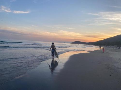 a man walking on the beach with a surfboard at Juquehy Casa Confort para Famílias em condomínio in Juquei