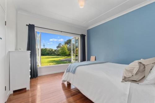 a bedroom with a bed and a large window at Somerton - Waipu Holiday Home in Waipu Cove