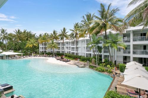 a swimming pool in front of a hotel with palm trees at Seascape Holidays at The Beach Club in Port Douglas