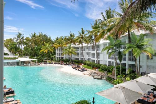 a swimming pool next to a beach with palm trees at Seascape Holidays at The Beach Club in Port Douglas
