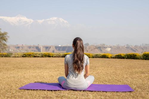 a woman sitting on a purple yoga mat in a field at Mountain Glory Forest Resort in Pokhara
