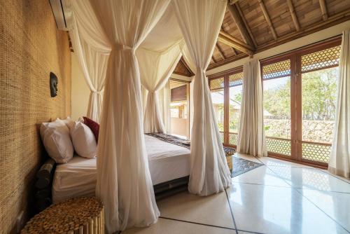 1 dormitorio con cama con cortinas y sofá en Maringi Sumba by Sumba Hospitality Foundation, en Waikelo