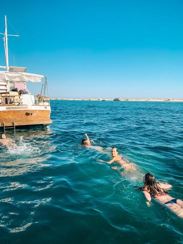 four people swimming in the water near a boat at Mulubinba SeaHouse in Olhão