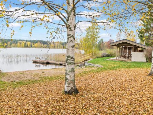a tree in front of a lake with a gazebo at Holiday Home Pihlajakumpu by Interhome in Petäjävesi