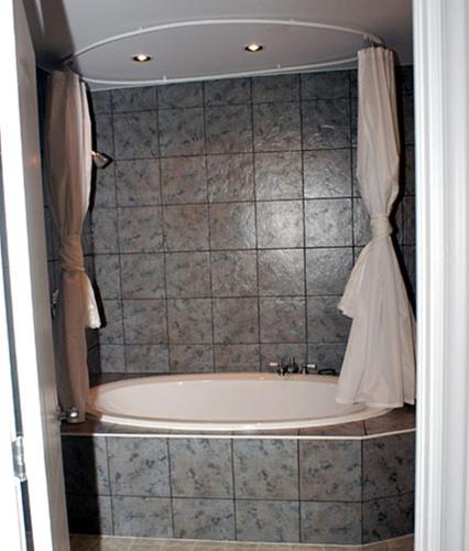 a bathroom with a tub with a shower curtain at Auberge Bay Wind Suites in Chéticamp