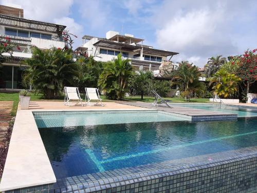 a swimming pool with two chairs and a building at Apartamentos no Pipa Residence in Pipa