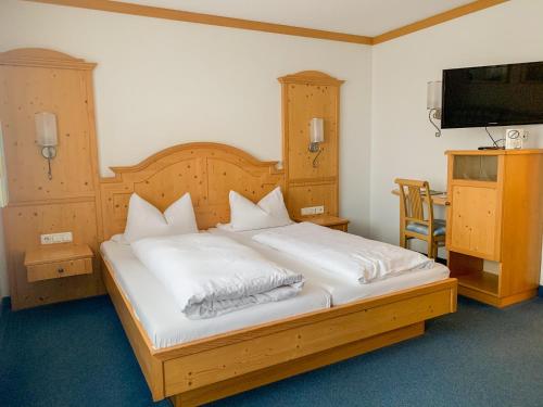 a bedroom with a bed with white sheets and a flat screen tv at Landhotel Bauernschmitt in Pottenstein