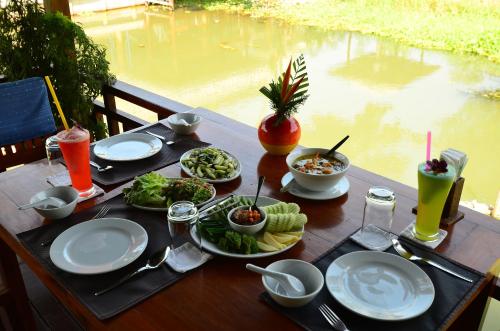 a wooden table with plates of food and drinks on it at Maikaew Damnoen Resort in Damnoen Saduak