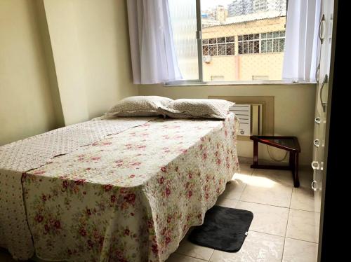 a bedroom with a bed with a flowered blanket and a window at Apto perto das praias do Flamengo e do Botafogo in Rio de Janeiro