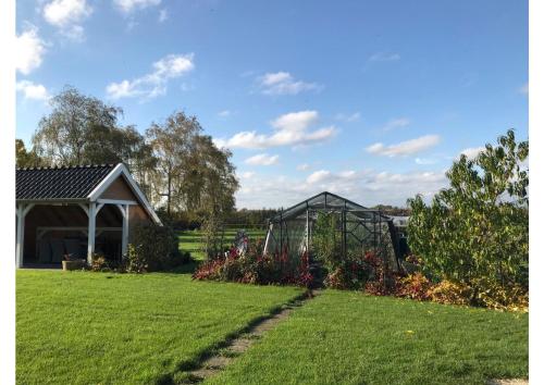 a garden with a greenhouse and some flowers at B&B De Spiegel - Genieten van rust en ruimte in Cothen