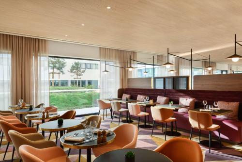 un restaurant avec des tables, des chaises et des fenêtres dans l'établissement Hyatt Place Paris Charles de Gaulle Airport, à Roissy-en-France