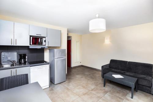 a living room with a black couch and a kitchen at SOWELL RESIDENCES Les Perles du Golfe de Saint-Tropez in Grimaud