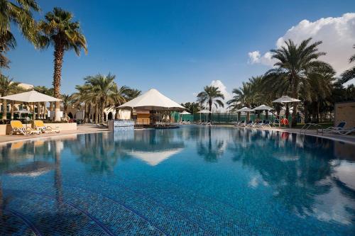 a large swimming pool with palm trees and umbrellas at Metropolitan Al Mafraq Hotel in Abu Dhabi