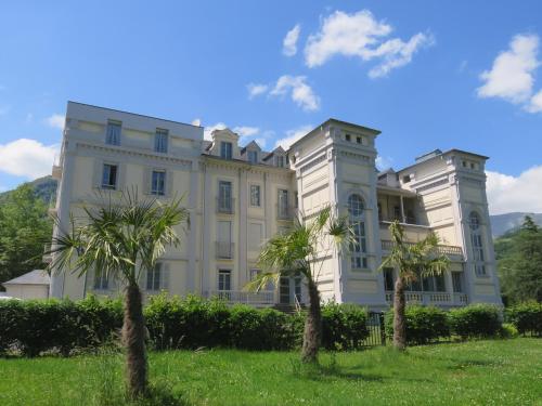 a large white building with palm trees in front of it at Le Balcon du Parc, entre Lourdes et Gavarnie in Argelès-Gazost