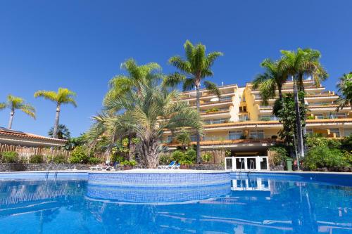 a swimming pool in front of a hotel with palm trees at Apartamentos Tigaiga Suites in Puerto de la Cruz