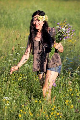 a woman walking through a field holding a bunch of flowers at Viesu nams RŪĶĪŠI in Rugāji