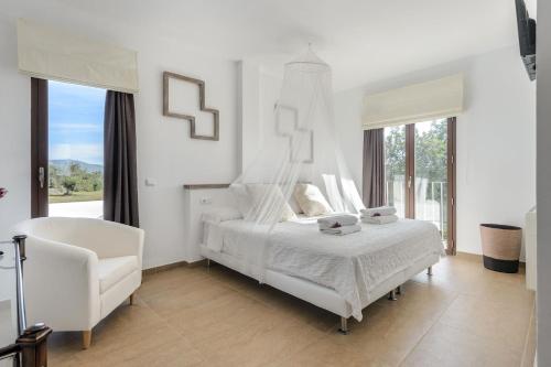 a white bedroom with a bed and a chair at Villa Can Lloren in Sant Llorenç de Balafia