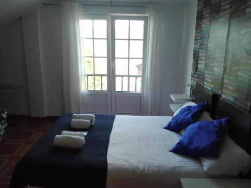 a bedroom with a large bed with blue pillows and a window at Hotel Corcubión Playa de Quenxe in Corcubión
