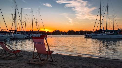 two chairs on the shore of a marina with boats at Przystań Tło dla Mew in Rydzewo