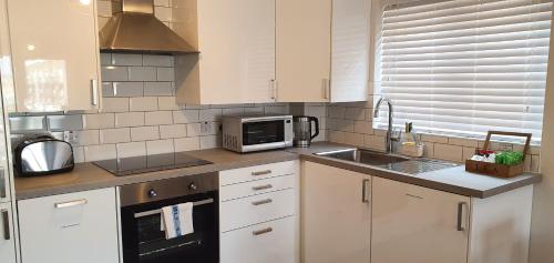 a kitchen with white cabinets and a sink and a microwave at Garland Modern Apartment Tilbury with Parking in Tilbury