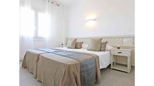 a white bedroom with a large bed and a table at Apartamentos Sema in Son Servera