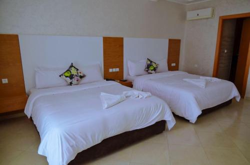 two beds in a hotel room with white sheets at Hotel SAHARATEL in Laayoune
