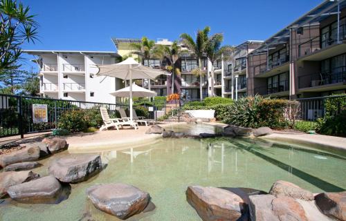 a pool with rocks and an umbrella and a building at The Beach Retreat Coolum in Coolum Beach
