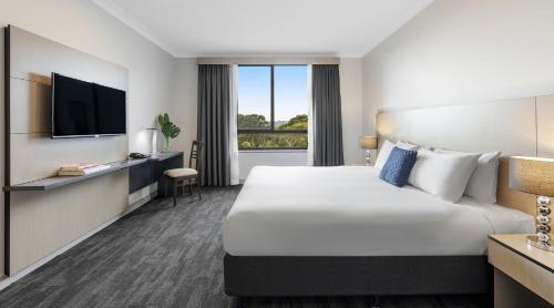 a hotel room with a large bed and a television at Oaks Sydney North Ryde Suites in Sydney