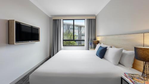 a hotel room with a large bed and a tv at Oaks Sydney North Ryde Suites in Sydney