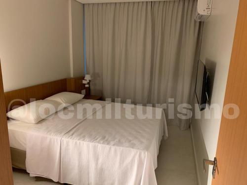 a bedroom with a white bed and a television at Apartamento em Resort - Exclusive in Salinópolis