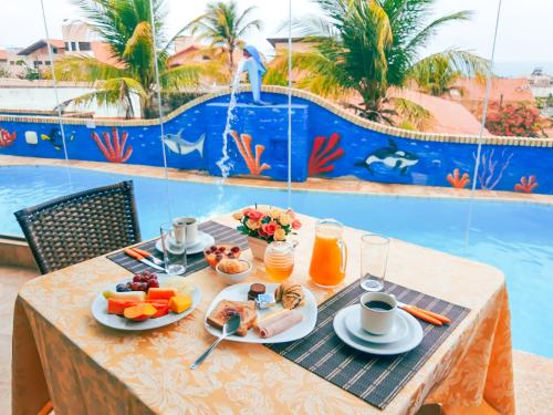 a table with breakfast food and a pool in the background at Planet Dunas Residence in Aquiraz