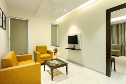 a living room with a couch and two chairs and a tv at Hotel Paramount Suites & Service Apartments in Mangalore
