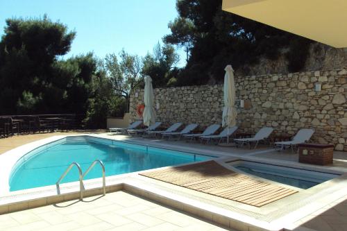 a swimming pool with chairs and a stone wall at Agrabeli Apartments in Limne
