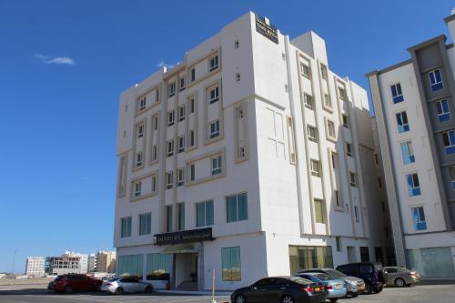Sama Muscat Hotel في Al Khawḑ: مبنى أبيض فيه سيارات تقف في موقف للسيارات