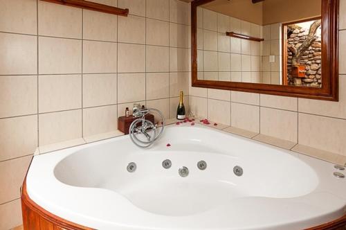 a large white tub in a bathroom with a mirror at Rain Farm Game Lodge in uMhlali