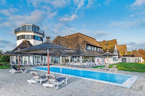 a house with a swimming pool with chairs and umbrellas at Hotel und Spa Lundenbergsand in Simonsberg